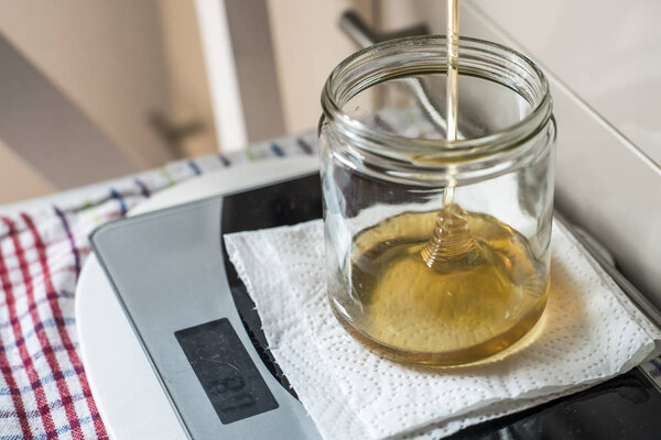 Beekeeper filling up the fresh golden new honey into glass jars on a scale scales