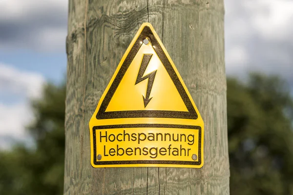 Tysk hög spänning skylt trä lodstaven med gröna träd i bakgrunden — Stockfoto