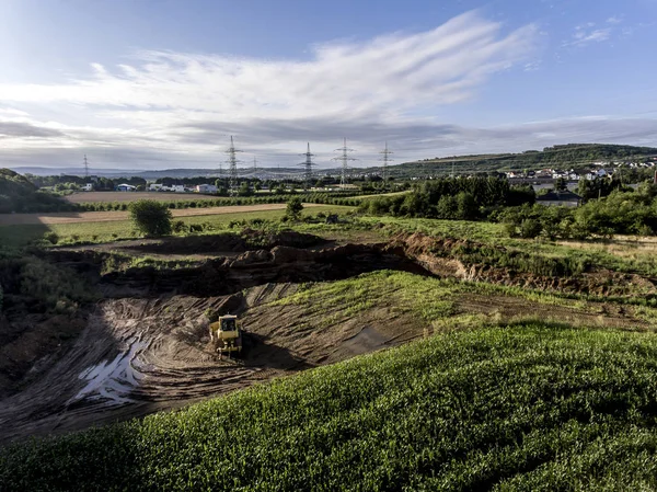 Ovanifrån tunga maskinen grävmaskin bagger arbetar i lera på byggarbetsplatsen med gröna landskapet kring — Stockfoto