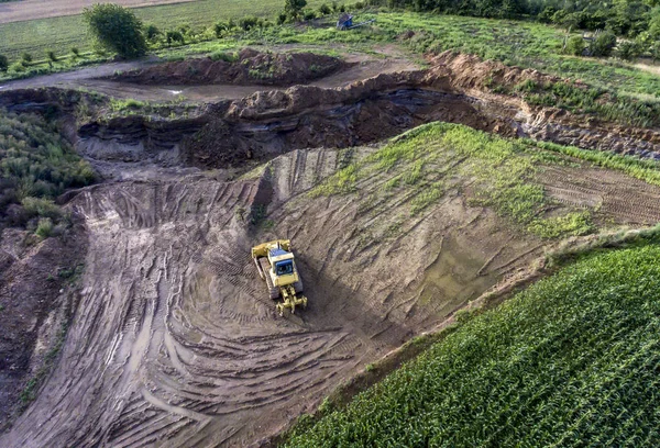 Bovenaanzicht zware machine graafmachine bagger werken in modder op de bouwplaats met groene landschap rond — Stockfoto