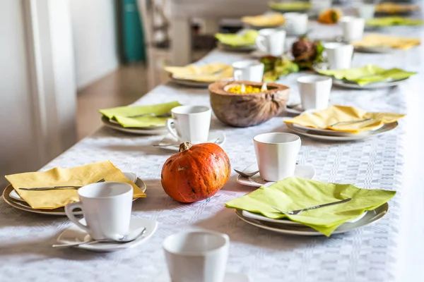 Beautiful festive dinner table colorful yellow fall helloween pumpkin decoration coffee mugs saucers plates and spoons — Stock Photo, Image