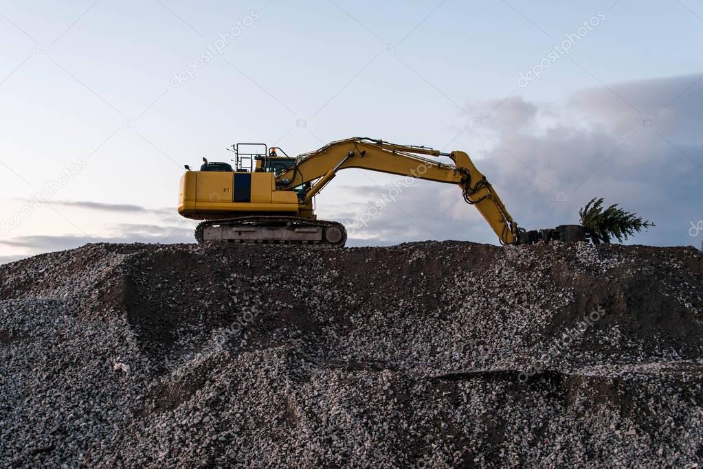 heavy machine excavator bagger on top of gravel construction site holding a green christmas tree