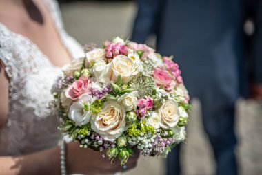 Gelin tarafından yakın planda tutulan bir buket çiçek. Pembe ve sarı güller