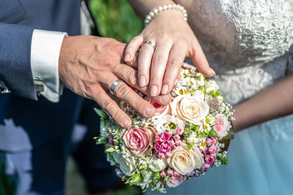 Mãos noivo e noiva com anéis de casamento e flores do buquê de casamento celebração símbolo do amor — Fotografia de Stock