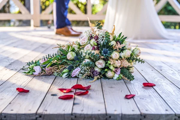 Wedding bouquet in front of newlyweds wedding couple inbackground, kissing or holding hands in love Shallow depth bokeh — Stock Photo, Image