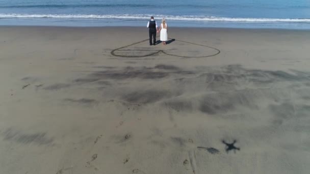 Foto aérea de pareja de vestidos de novia en la playa tropical Playa Arenillas en Costa Rica con un corazón atraído por la arena — Vídeos de Stock