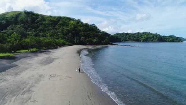 Aerial shot of wedding dress couple on the tropical beach Playa Arenillas in Costa Rica with a heart drawn into Sand — Stock Video