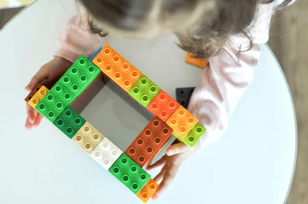 Kind spelen met plastic kleurrijke blokken constructeur op de kleuterschool. Close-up van kleine meisje handen gebouw met kleurrijke constructie thuis. Klein meisje met educatief speelgoed blokken op de kleuterschool — Stockfoto