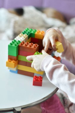 Plastik renkli blok yapımcısıyla oynayan bir çocuk. Evinde renkli bir inşaat olan küçük kız el binasını kapatın. Eğitici oyuncakları olan küçük bir kız.