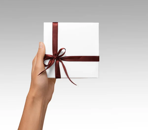 Isolato donna mani che tengono vacanze regalo scatola bianca con nastro marrone su uno sfondo bianco — Foto Stock