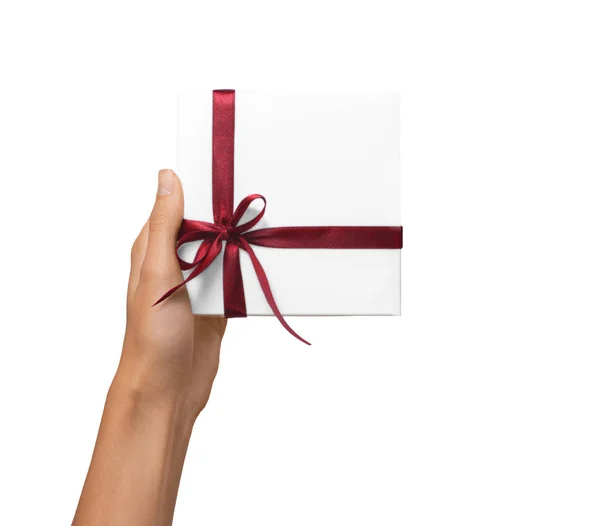 Las manos aisladas de la mujer que sostienen la caja blanca del regalo de vacaciones con la cinta roja en un fondo blanco — Foto de Stock
