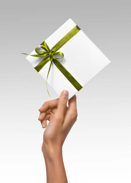 Las manos aisladas de la mujer que sostienen la caja blanca del regalo de vacaciones con la cinta verde en un fondo blanco — Foto de Stock