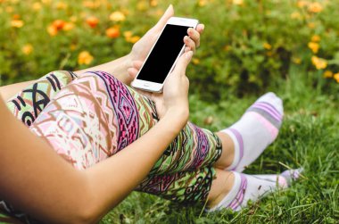 şık, trendy kadın ellerinde çiçeklerle yeşil çim zemin üzerine beyaz cep telefonunuzu bir egzersiz molası sırasında kapatın