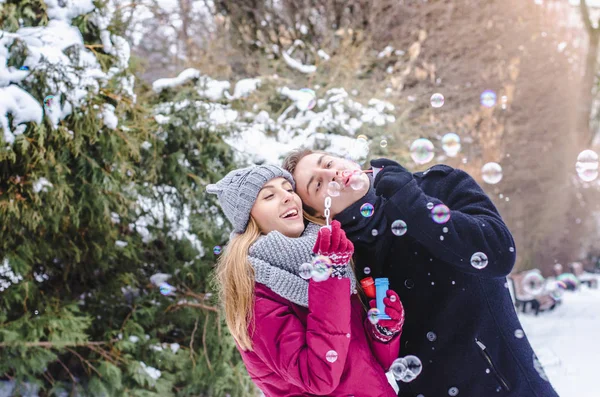 Romantische paar verliefd blazen van zeepbellen, samen plezier in winter kleding buiten. Soep bubbels. — Stockfoto