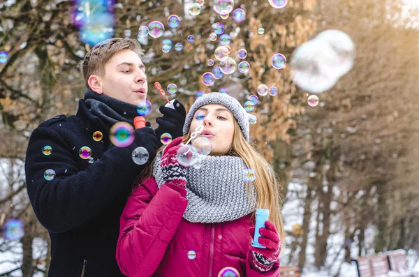 Romantische paar verliefd blazen van zeepbellen, samen plezier in winter kleding buiten. Soep bubbels. — Stockfoto