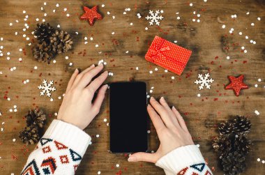 Noel hediye kar taneleri ve kar ile ahşap arka plan üzerinde akıllı cep telefonu ile oled göstermek tutarak sıcak örme kazak kadın elinde. Mutlu yeni yıl ve Xmas düz kompozisyon üstten görünüm yatıyordu.