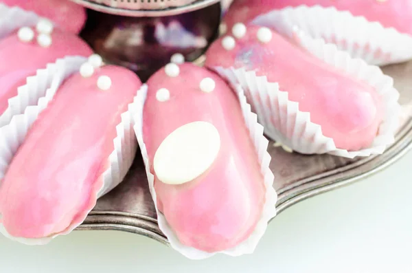 Elegant french pastry glazed pinc eclairs decorated with white edible balls and a medallion of white chocolate for the company\'s inscription or copy space on a silver plate on a white background.