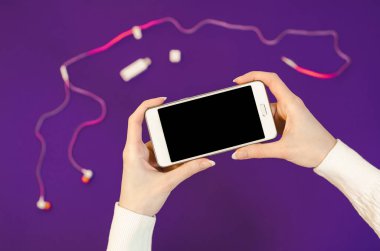 Eller yıl arka plan aksesuarları kulaklık ultra mor renk oled ekranlı akıllı cep telefonu tutan cep telefonu kullanarak bir sıcak beyaz kazaklı kadın. Düz yatıyordu bussines kompozisyon Üstten Görünüm iletişim kapatın