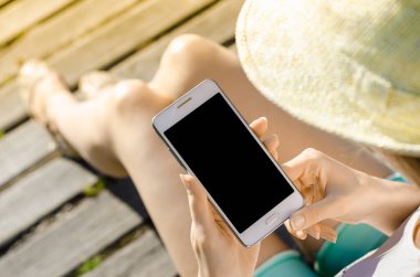 Yakın kadar iş kadını şapka kullanma Smartphone cep telefonu açık siyah Oled ekran ahşap arka plan şık yaz giyinmiş hipster içinde