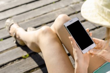 Yakın kadar iş kadını şapka kullanma Smartphone cep telefonu açık siyah Oled ekran ahşap arka plan şık yaz giyinmiş hipster içinde