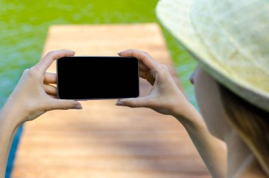 Yakın kadar iş kadını şapka kullanma Smartphone cep telefonu açık siyah Oled ekran ahşap arka plan şık yaz giyinmiş hipster içinde