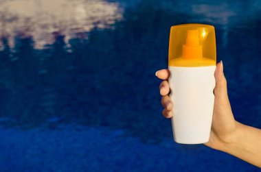 Güneş koruma su arka plan üzerinde krem ile eller. Cilt bakım kavramı güneş koruyucu sprey şişe losyon kozmetik ürünleri.