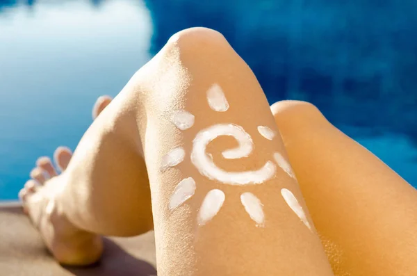 Young woman with sun shape on the leg holding sun protection cream bottle on the beach near swimming pool blue water rest calm view sunscreen cosmetics products