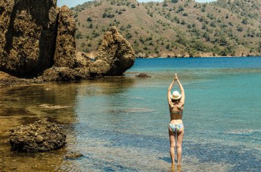Genç gülümseyen kadın güzel spor ince rakam içinde mavi su turkuaz lagün görünümü ada kayalık kıyılarında ayakta özgürlük egzersiz yoga yaparken swimsuite yazın sağlıklı tatil