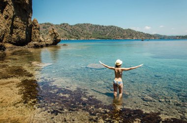 Genç gülümseyen kadın güzel spor ince rakam içinde mavi su turkuaz lagün görünümü ada kayalık kıyılarında ayakta özgürlük egzersiz yoga yaparken swimsuite yazın sağlıklı tatil