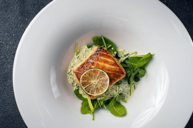 Limonlu ve otlu ızgara somon bifteği, beyaz tabakta, siyah arka planda. Yiyeceğe bak. Üst görünüm, alanı kopyala.