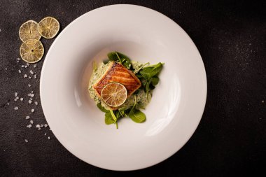 Limonlu ve otlu ızgara somon bifteği, beyaz tabakta, siyah arka planda. Yiyeceğe bak. Üst görünüm, alanı kopyala.