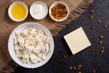 Beyaz tabakta süzme peynir, ayrı ayrı bal, koyu arkaplandaki notlar için yapraklı kuru üzüm. Üst görünüm.