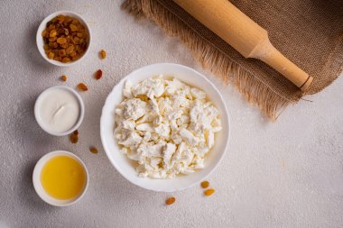 Beyaz tabakta süzme peynir, ayrı ayrı bal, beyaz arka planda kuru üzüm. Sağlıklı yiyecekler. Üst görünüm.