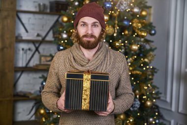 Noel ve yeni yıl Noel ağacı arka plan sakallı modeli şık kazaklı partisi için sürpriz bir hediye elinde olan yakışıklı adam verir