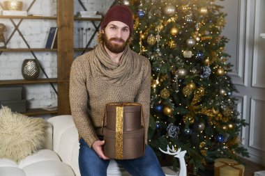 Genç adam oturur Noel ağacı arasında kanepede moda ve kameraya el kız arkadaşı veya karısı için verdiği hediye görünüyor