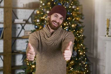 Onun yüz ve jest büyük bir başparmak mutlu bir ifade. Noel ve yeni yıl onuruna bir tatil atmosferini. Sıcak bir dekora sahip rahat iç. Büyük hediye ya da satın alıyor. Bir şekilde dekore edilmiş ağaç.