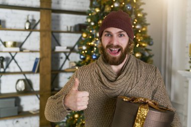 güçlü samimi duygu. mutluluk ifadesi. Noel ve yılbaşı için hediye çarpıcı. Hediyelik Noel ağacı arka planda tutarak yukarı başparmak. Harika parti konsept.