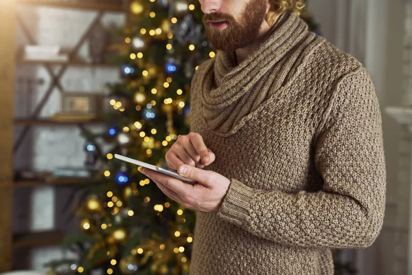 Christmas man on tablet doing internet shopping or shearing with friends. Young male model excited about buying gifts online on his modern tablet. Christmas or New Year. Thinking about gift concept
