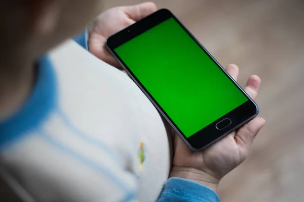 The child is holding a phone in his hand with a green screen for chroma keyer — Stock Photo, Image