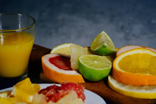 さまざまな柑橘系の果物は、スライス オレンジ、レモン、ライム、グレープ フルーツ、ザボン、オレンジ ジュースのガラスにカット。木の板と自然木材テクスチャの背景にビンテージ ホワイト プレート上に広がって. — ストック写真