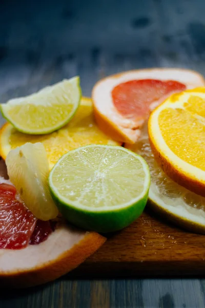 Varios cítricos cortados en rodajas naranja, limón, lima, pomelo. Extiende sobre una tabla de madera sobre un fondo vintage de textura de madera natural . — Foto de Stock