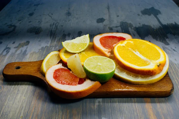 Divers agrumes coupés en tranches orange, citron, citron vert, pamplemousse, pomelo. Étalé sur une planche de bois sur un fond vintage de texturation du bois naturel . — Photo