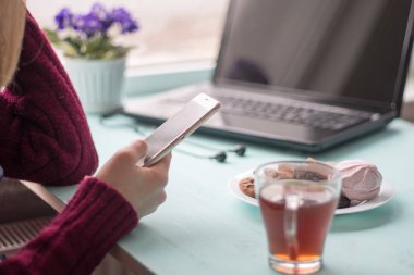 Pazar sabahı kafede içki içen ve cep telefonu kullanan genç bir kadın.