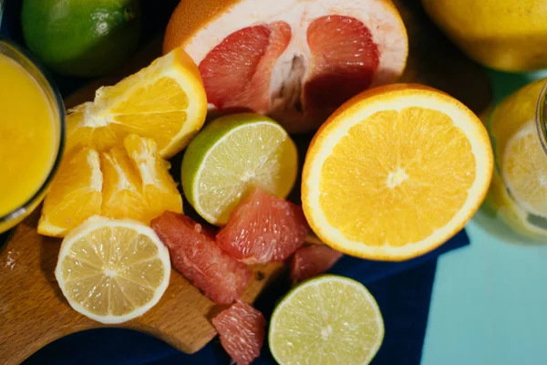 Cítricos, naranjas, limones, limas, pomelo sobre tabla vintage, limonada y zumo en un vaso de vidrio sobre fondo turquesa — Foto de Stock