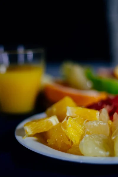 Varios cítricos cortados en rodajas naranja, limón, lima, pomelo, pomelo y un vaso de jugo de naranja. Extendido sobre una tabla de madera y un plato blanco vintage sobre el fondo de la textura de madera natural . — Foto de Stock