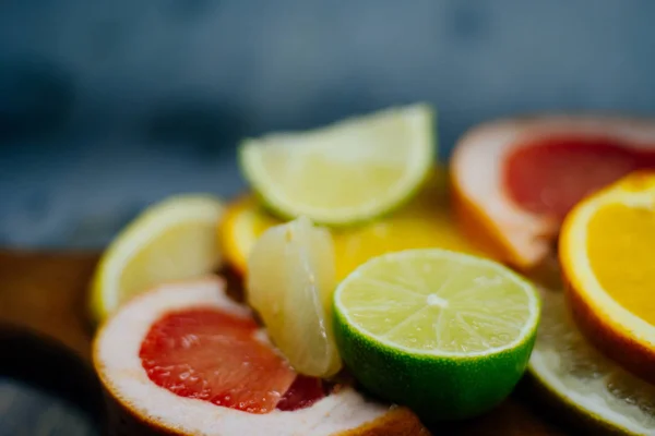 Varios cítricos cortados en rodajas naranja, limón, lima, pomelo. Extiende sobre una tabla de madera sobre un fondo vintage de textura de madera natural . — Foto de Stock