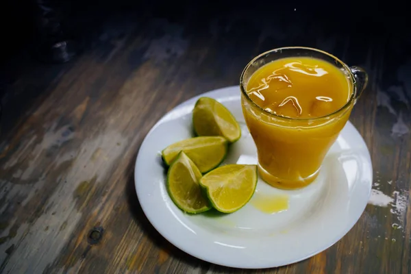 Стакан апельсинового сока с большим брызгом и лаймом на тарелке — стоковое фото