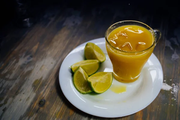 A glass of orange juice With a big splash and lime on a plate — Stock Photo, Image