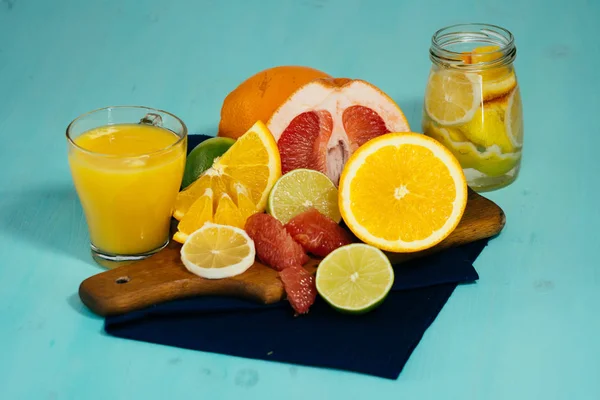 Citrus, oranges, lemons, limes, grapefruit, pomelo on vintage board, lemonade and juice in a glass of glass on a turquoise background