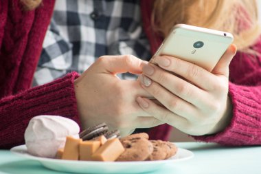 Pazar sabahı kafede içki içen ve cep telefonu kullanan genç bir kadın.
